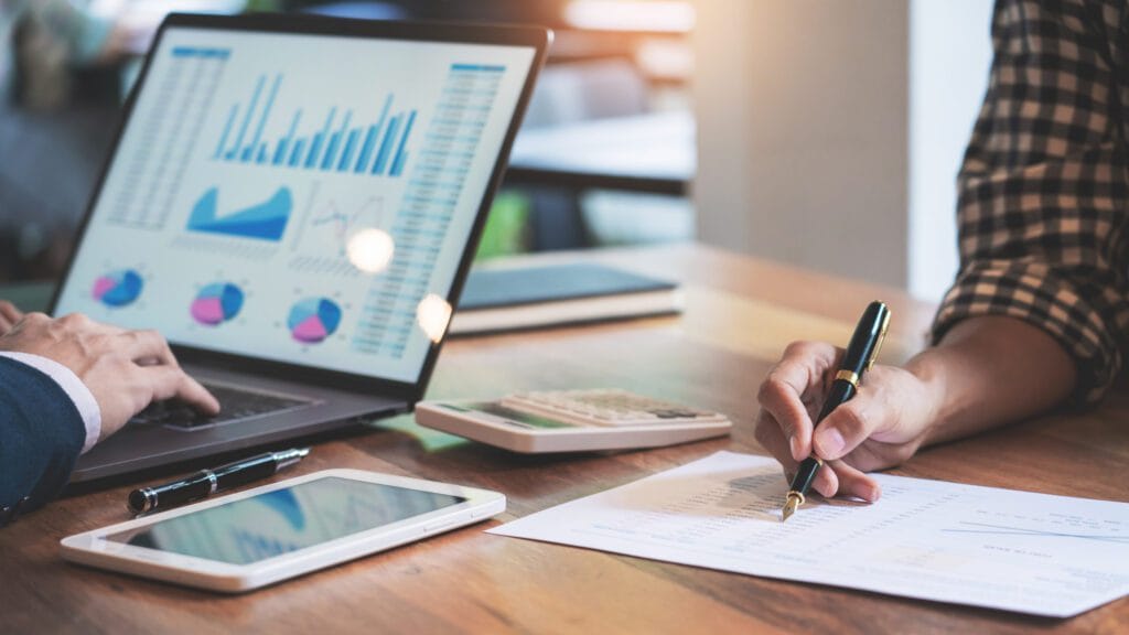 Pessoas analisando gráficos no laptop e documentos financeiros, simbolizando o BPO Financeiro e a gestão de dados para tomada de decisão estratégica.
