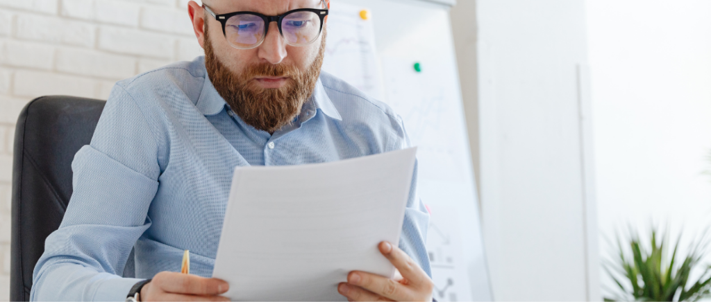 A imagem mostra um homem lendo com atenção alguns papéis, representando o dono de uma empresa analisando o que muda com a Lei n.º 15.270/2025. Com isso, ele pode se preparar para adequar o que for necessário.